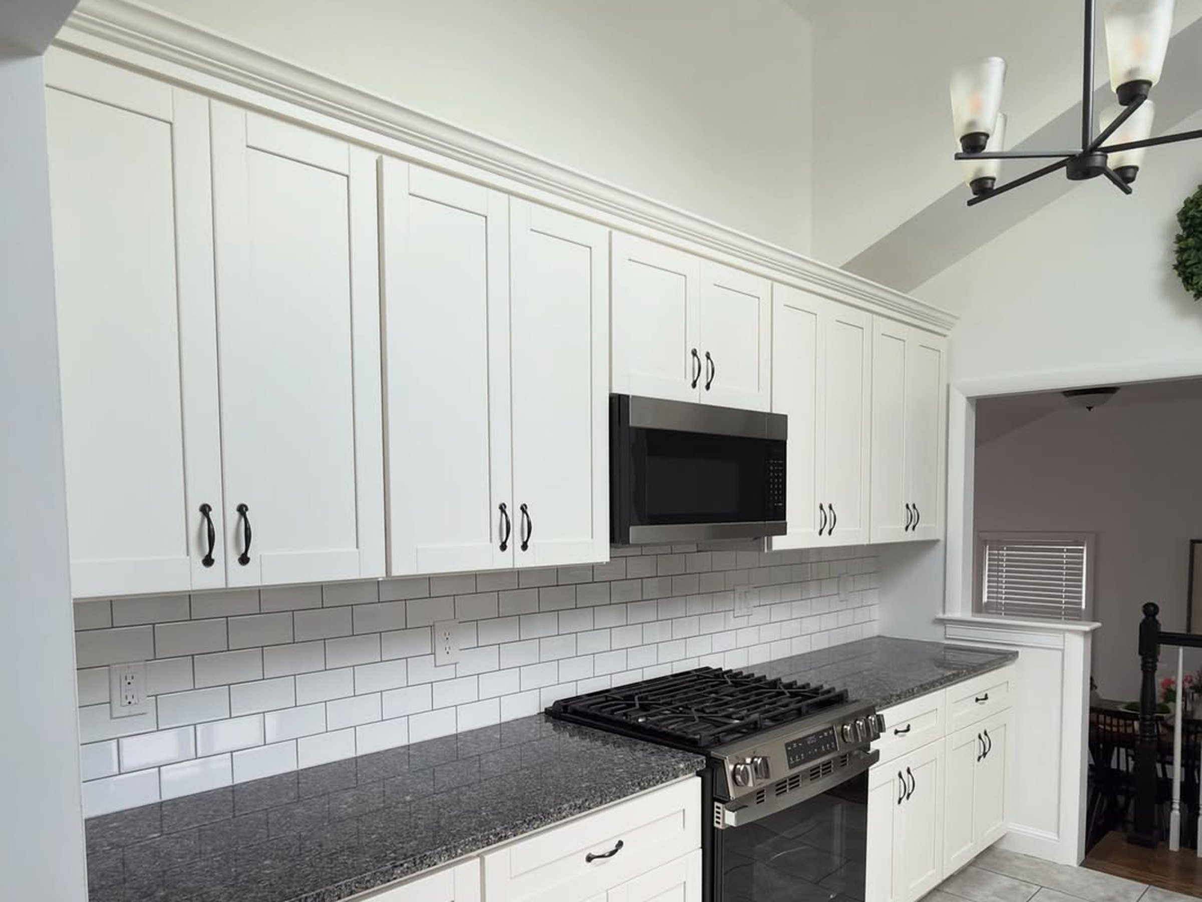 White shaker kitchen cabinets professionally painted by Pedretti's Cabinet Co., with dark granite countertops and a subway tile backsplash